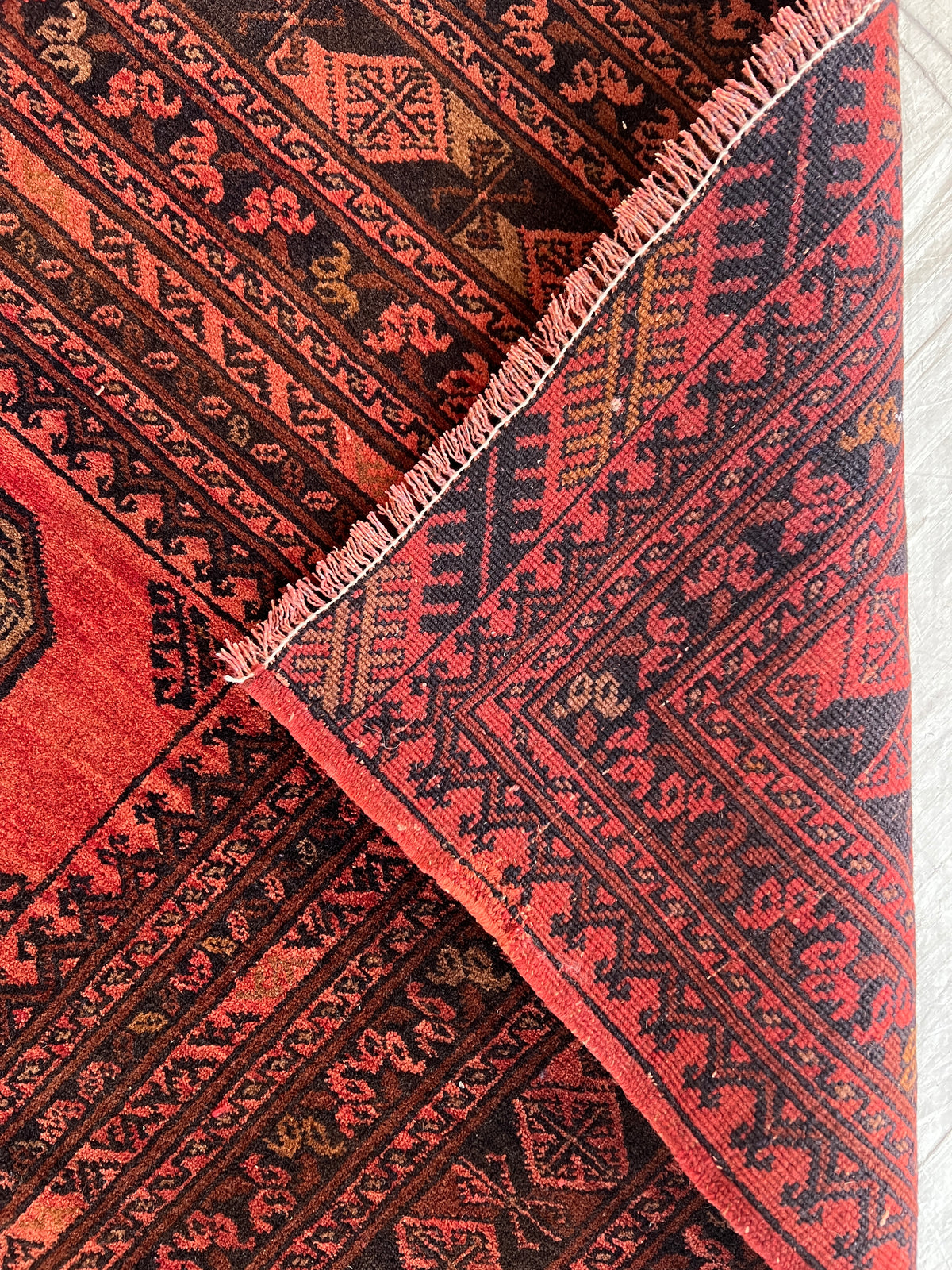 Close-up of a patterned red and black rug with fringed edge.